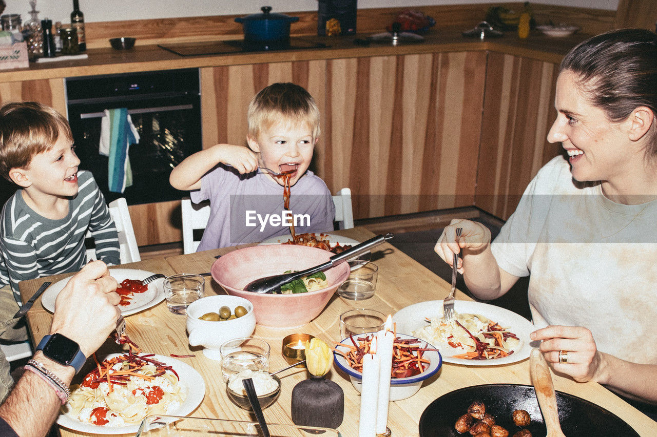 Playful kids having meal with parents while sitting at dining table in home