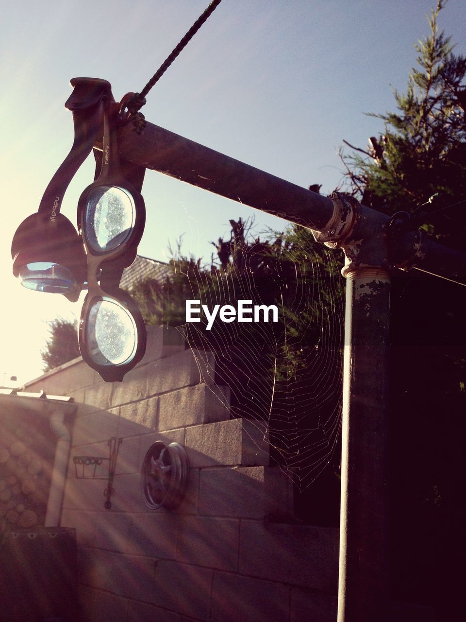 Sunlight falling on swimming goggles and spider web on pipe against sky