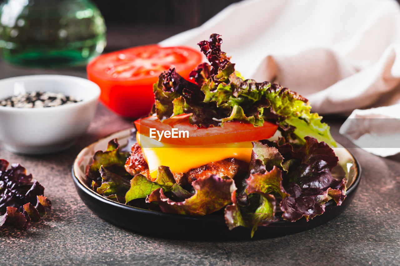 Spicy keto burger on fresh lettuce leaves of cutlet, tomato and cheese on a plate on the table