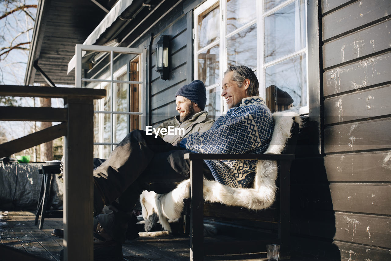 Happy mature friends sitting together at front porch in winter