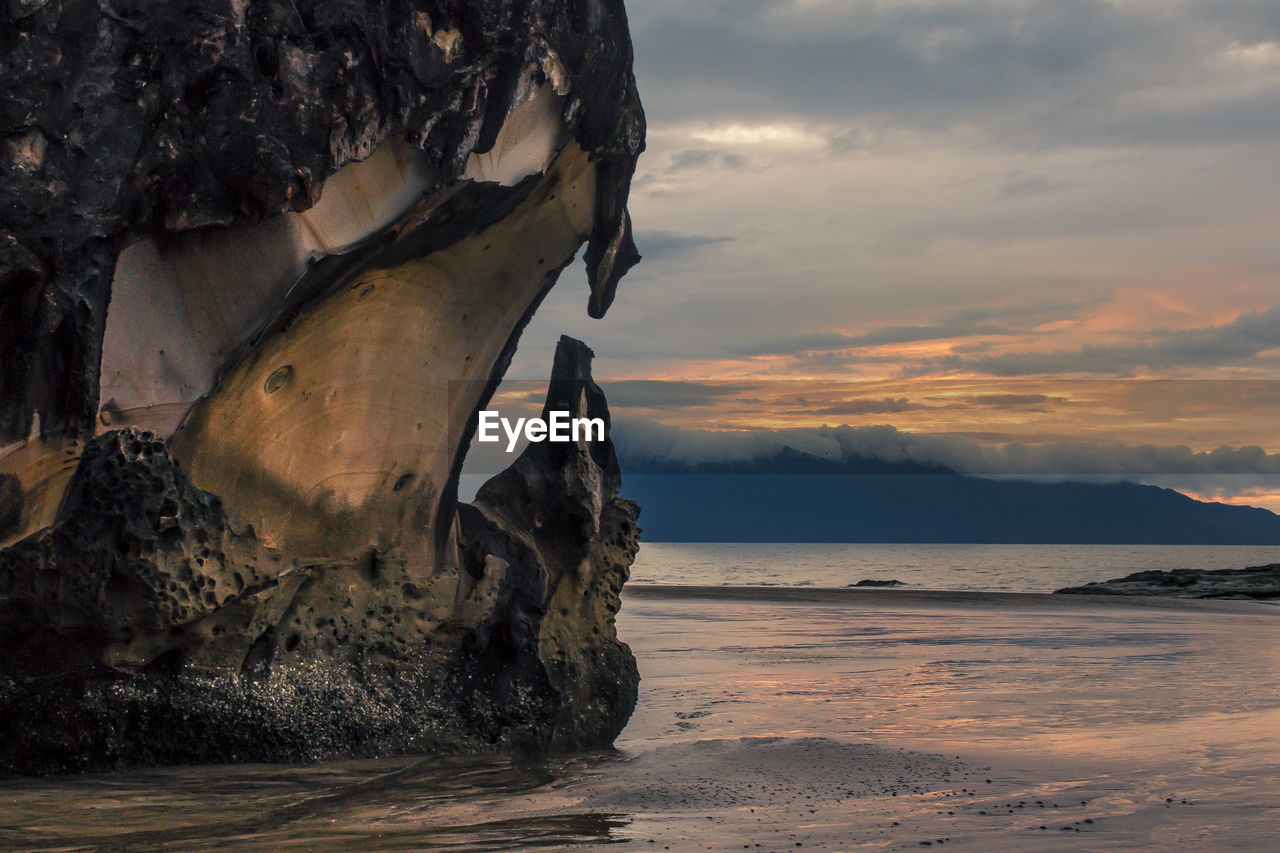 Rock formation on beach against sky during sunset