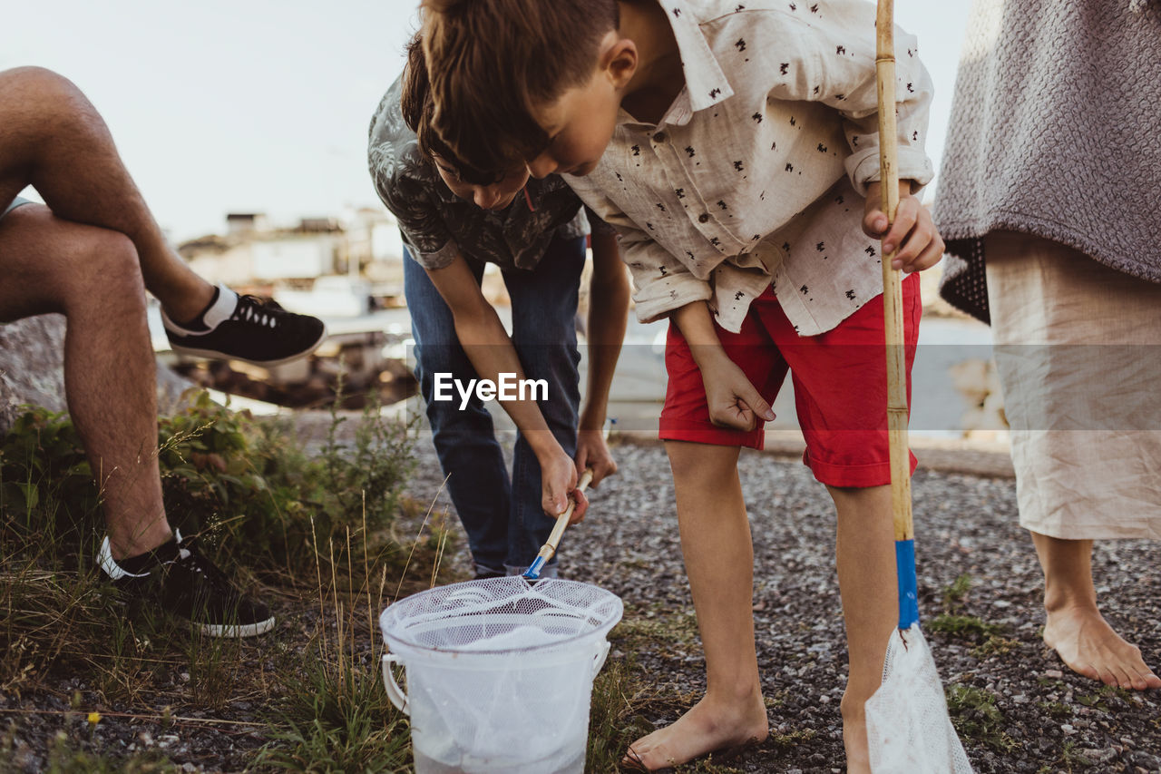 Brother looking at bucket through fishing net while bending by sibling over archipelago