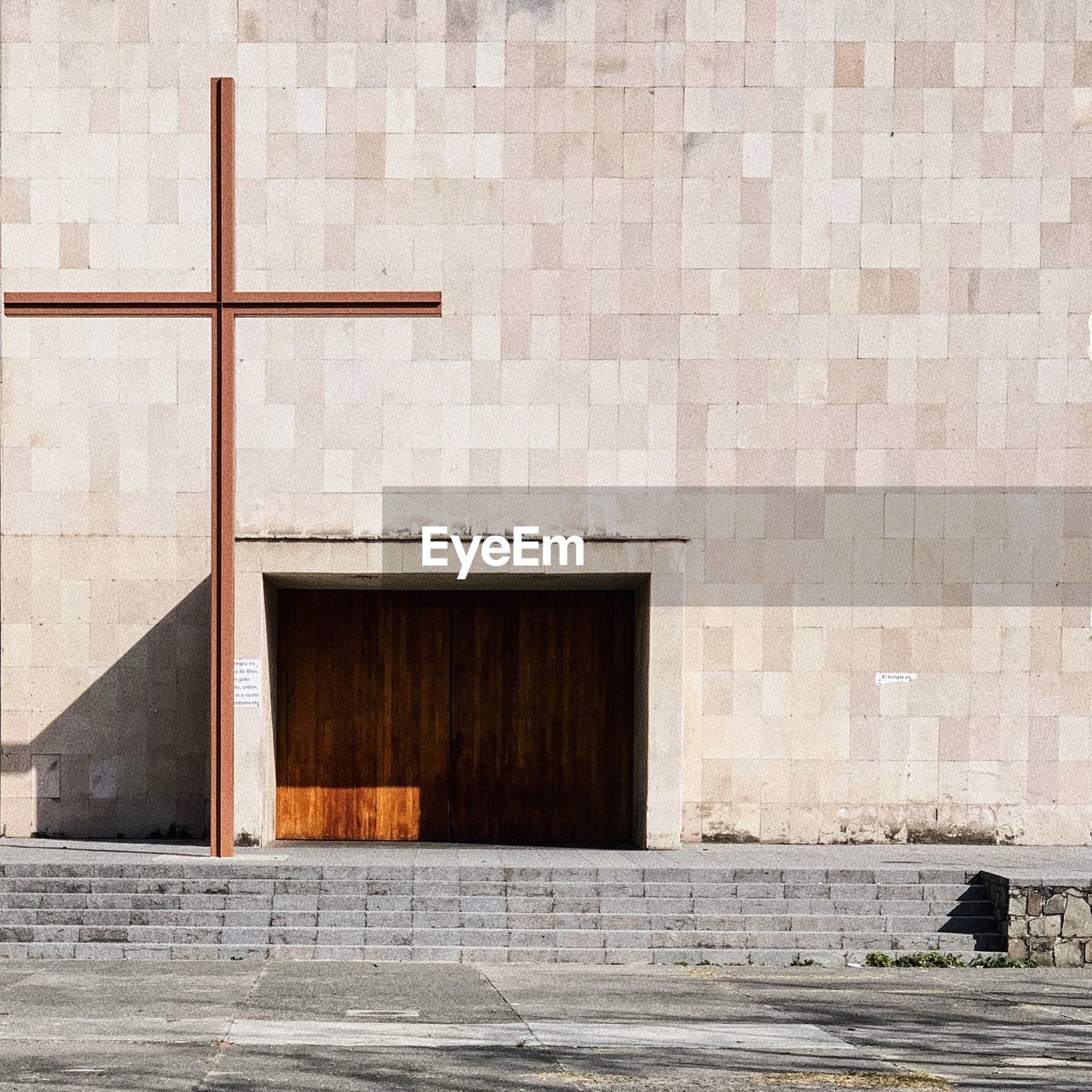 Religious cross on footpath against wall of building