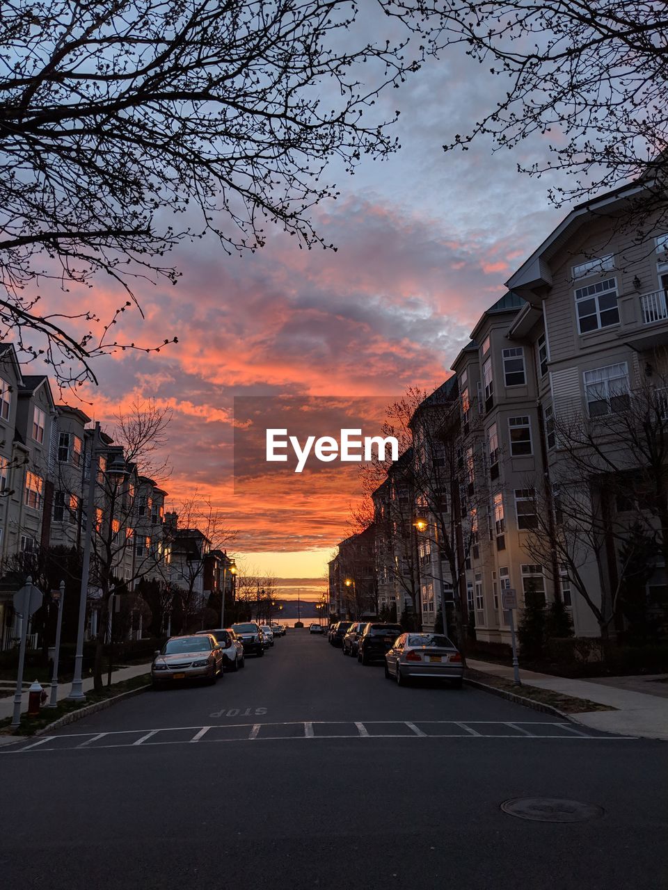 CARS ON STREET AMIDST BUILDINGS AGAINST SKY DURING SUNSET