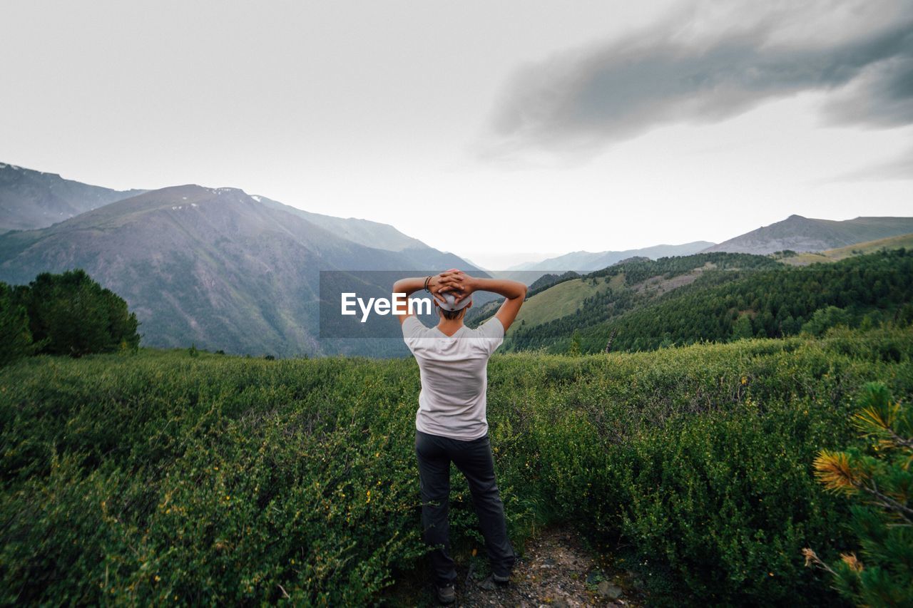 FULL LENGTH OF MAN STANDING ON GRASS AGAINST MOUNTAIN