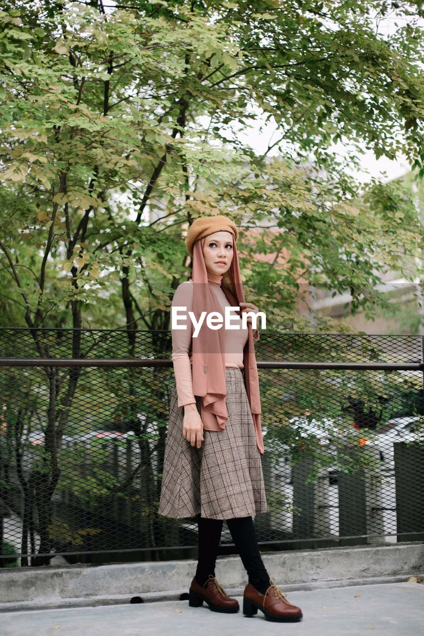 Woman looking away while standing against railing and trees