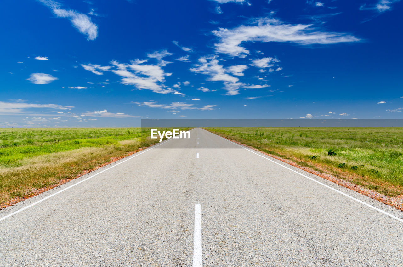 Road amidst green landscape against blue sky