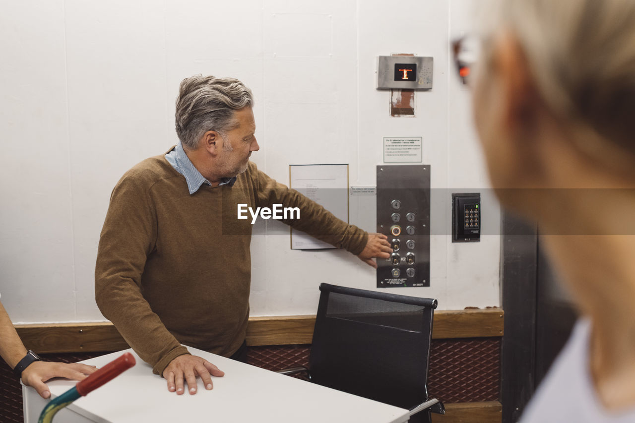 Mature businessman pressing elevator button while moving into new office