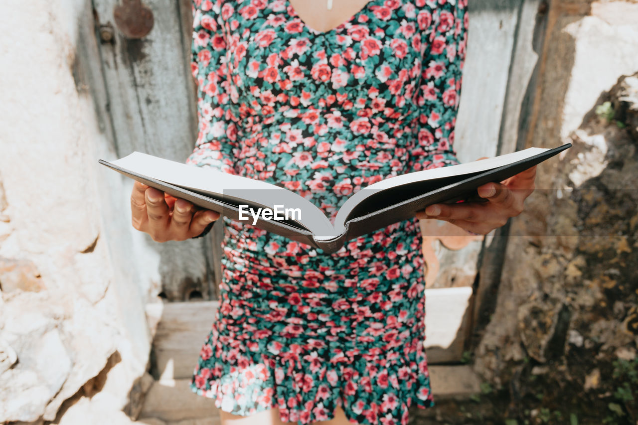 Midsection of woman holding book against wall