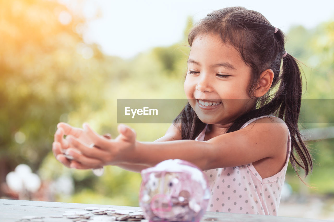 Girl putting coin in piggy bank at table