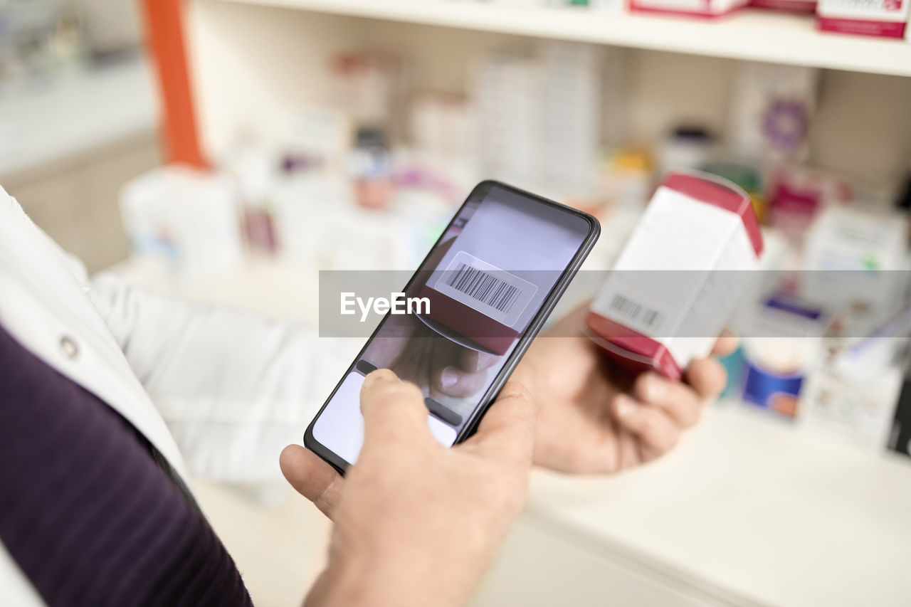 Pharmacist scanning barcode of medicine box through smart phone at pharmacy store