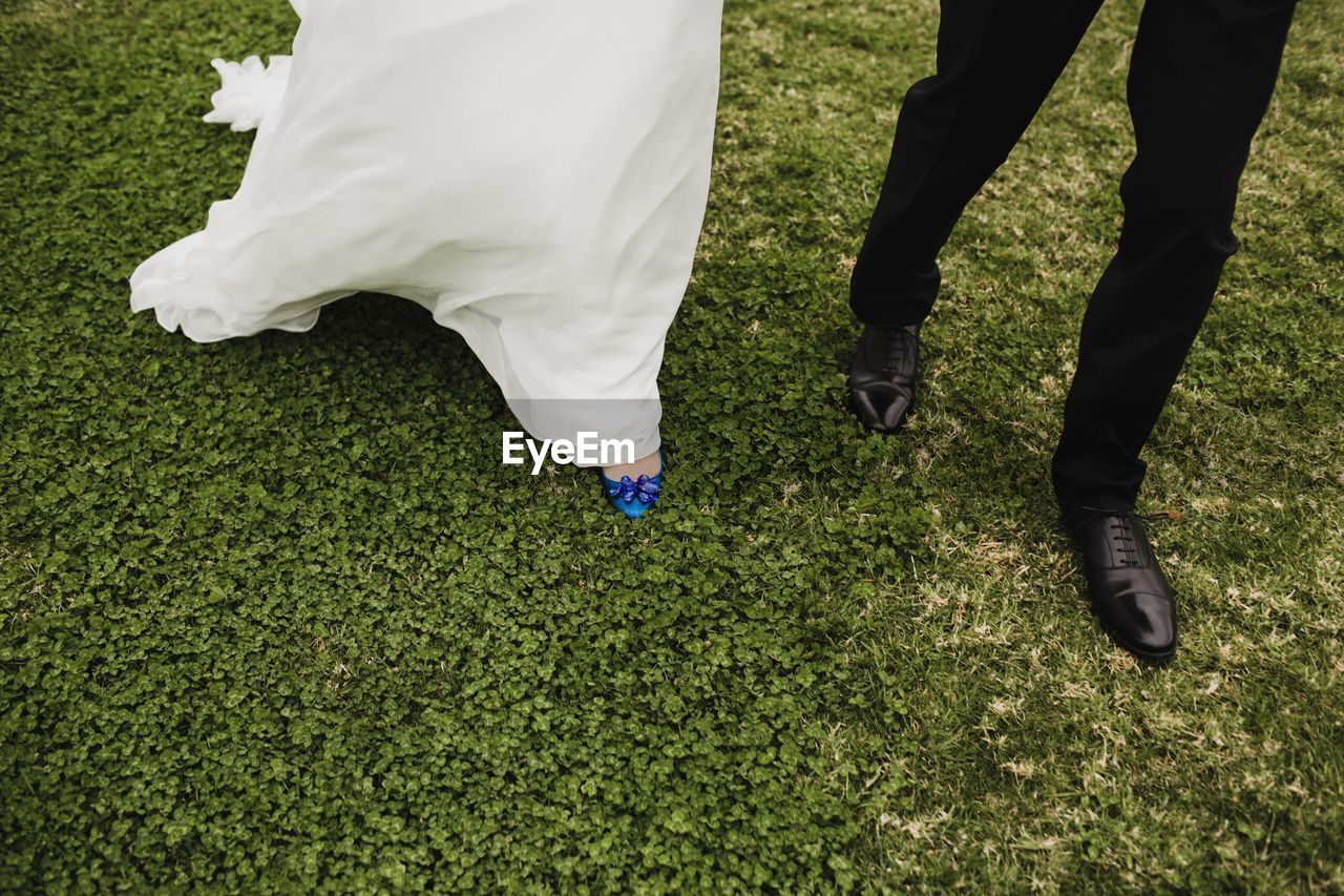 Low section of newlywed married couple walking on field