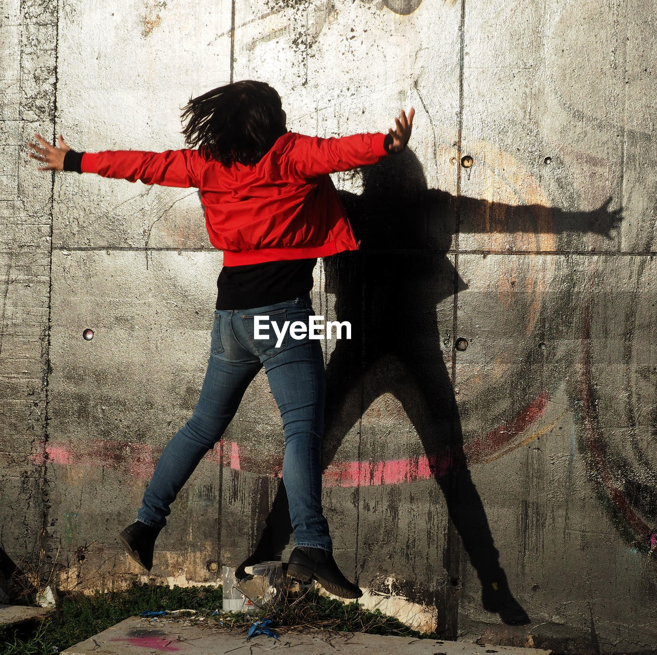 Woman jumping with arms outstretched against wall