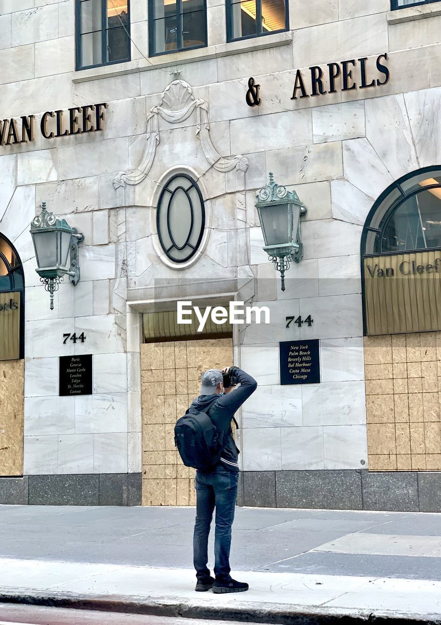 FULL LENGTH REAR VIEW OF MAN STANDING AGAINST BUILDING