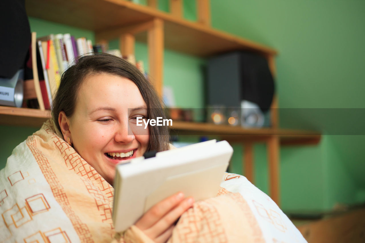 PORTRAIT OF SMILING WOMAN HOLDING MOBILE PHONE IN LAPTOP