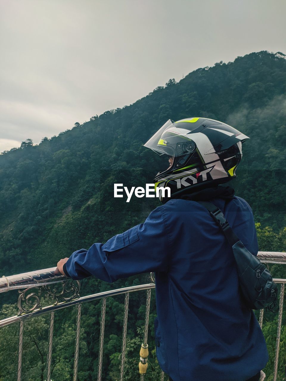 MAN STANDING BY RAILING AGAINST MOUNTAIN