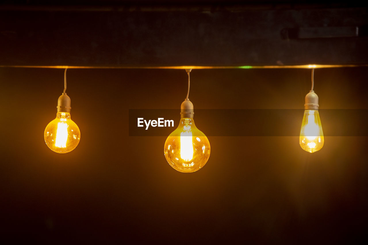 LOW ANGLE VIEW OF ILLUMINATED LIGHT BULB HANGING IN DARK