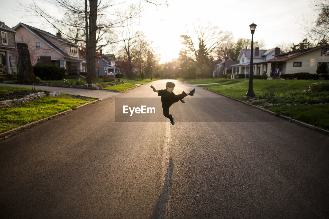 Full length of playful boy kicking in air while practicing karate on road during sunset