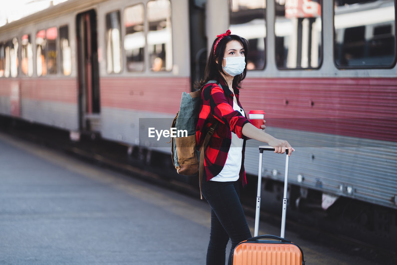 Young woman wearing mask standing by train