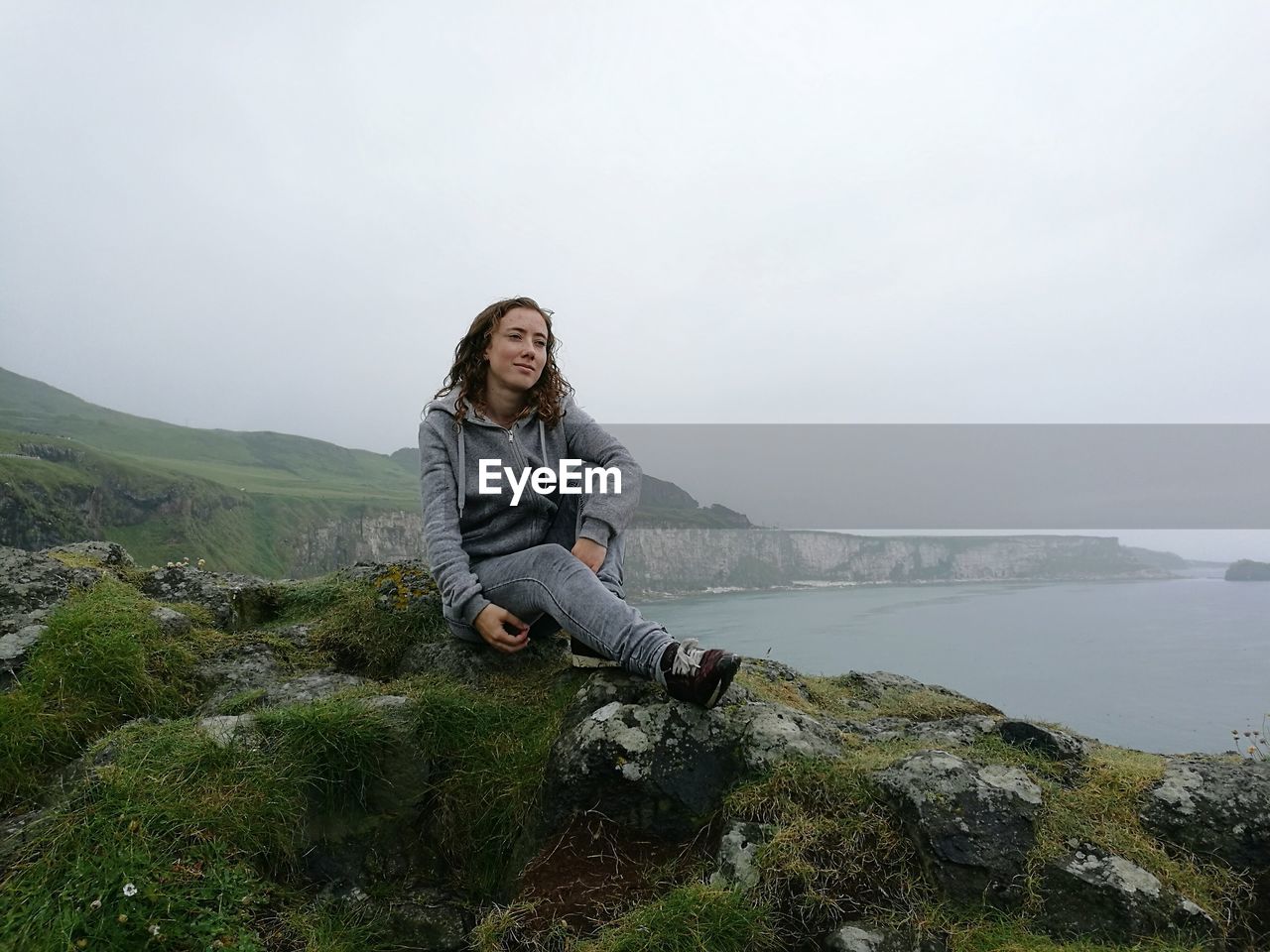 Young woman sitting on mountain at giant causeway against sky