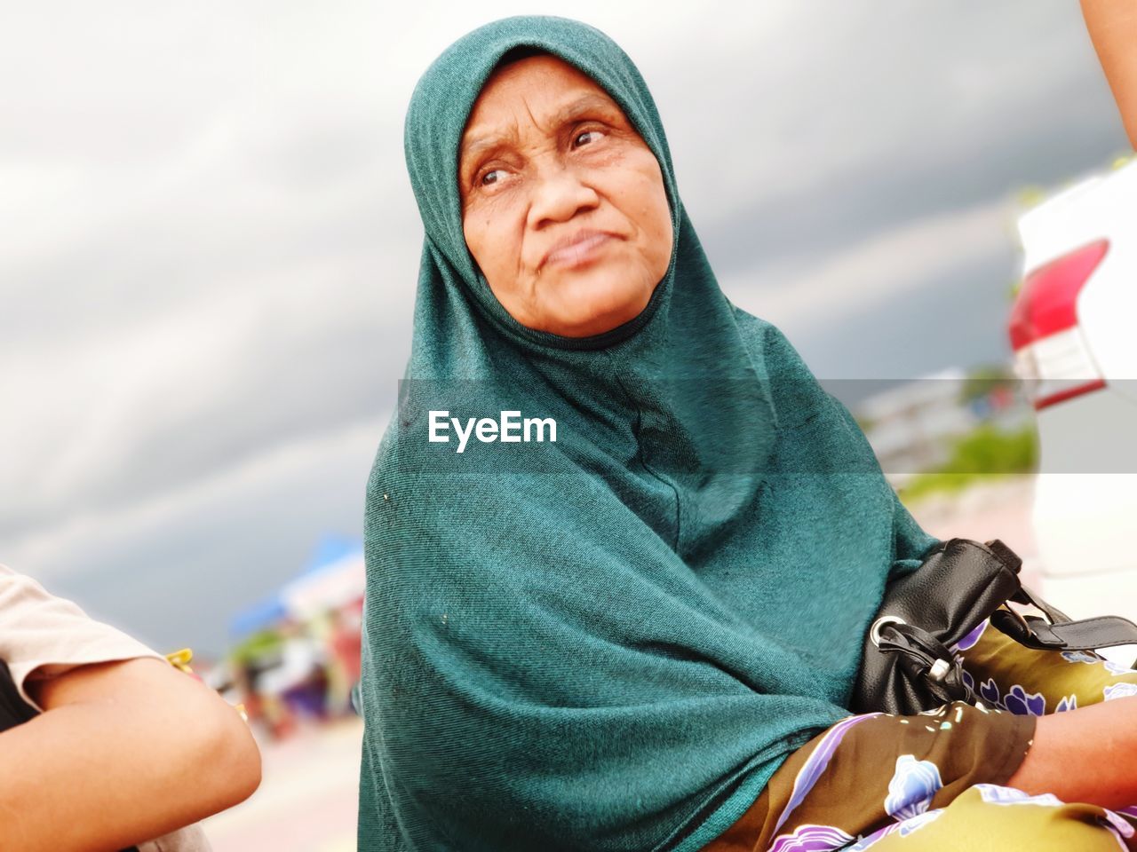 Low angle view of senior woman wearing hijab looking away against cloudy sky