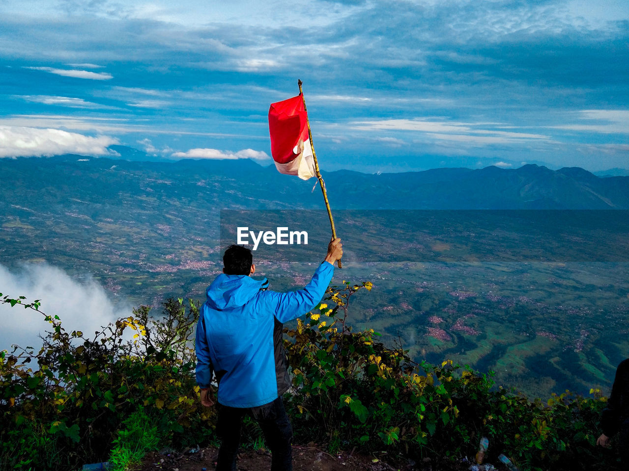 Rear view of man holding flag on cliff against mountain and sky