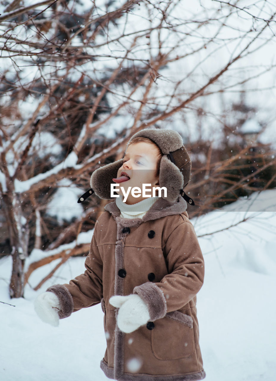 A boy in a winter hat and coat rejoices in the snow. the child catches snowflakes with his tongue. 