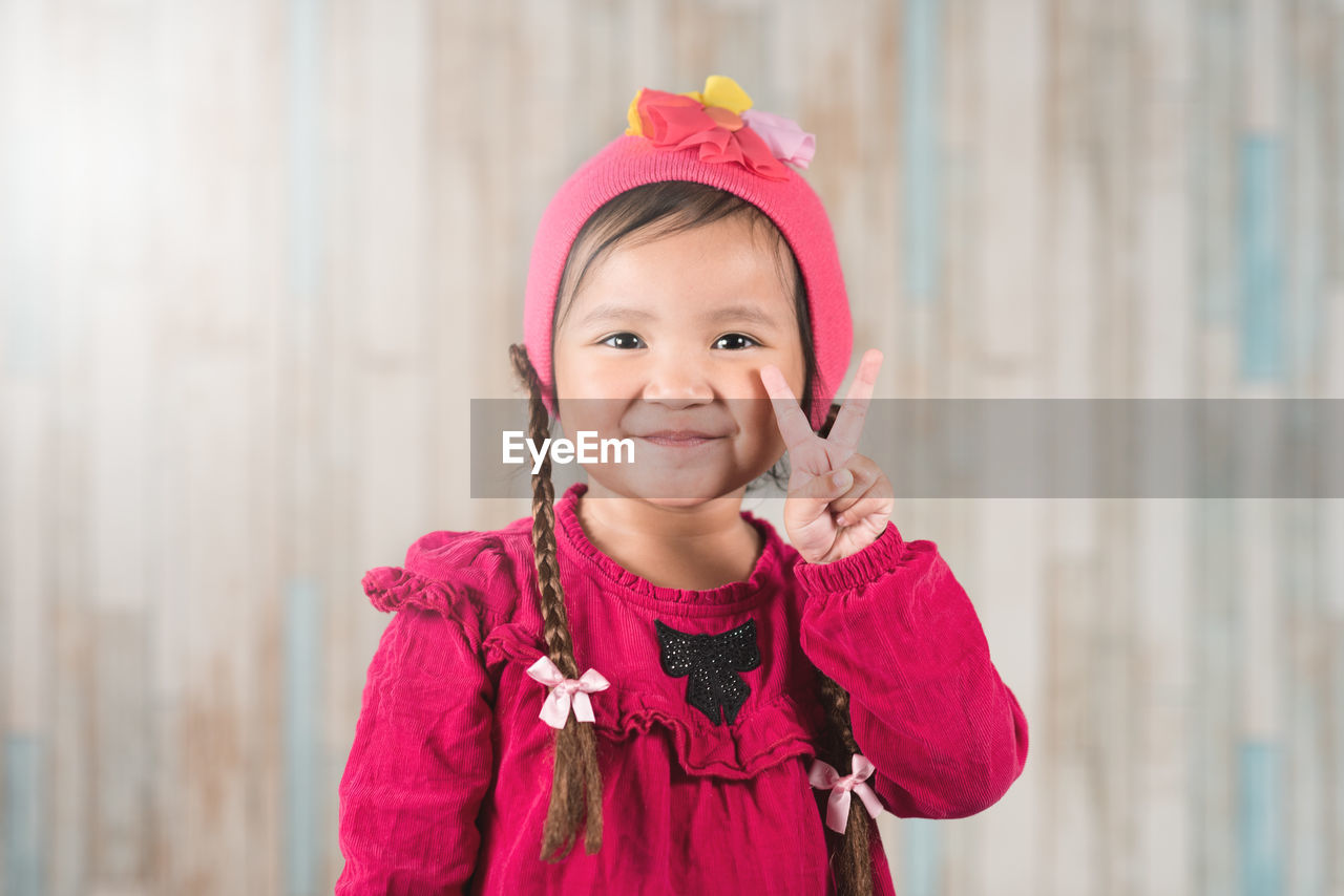 Portrait of smiling girl gesturing while standing against wall