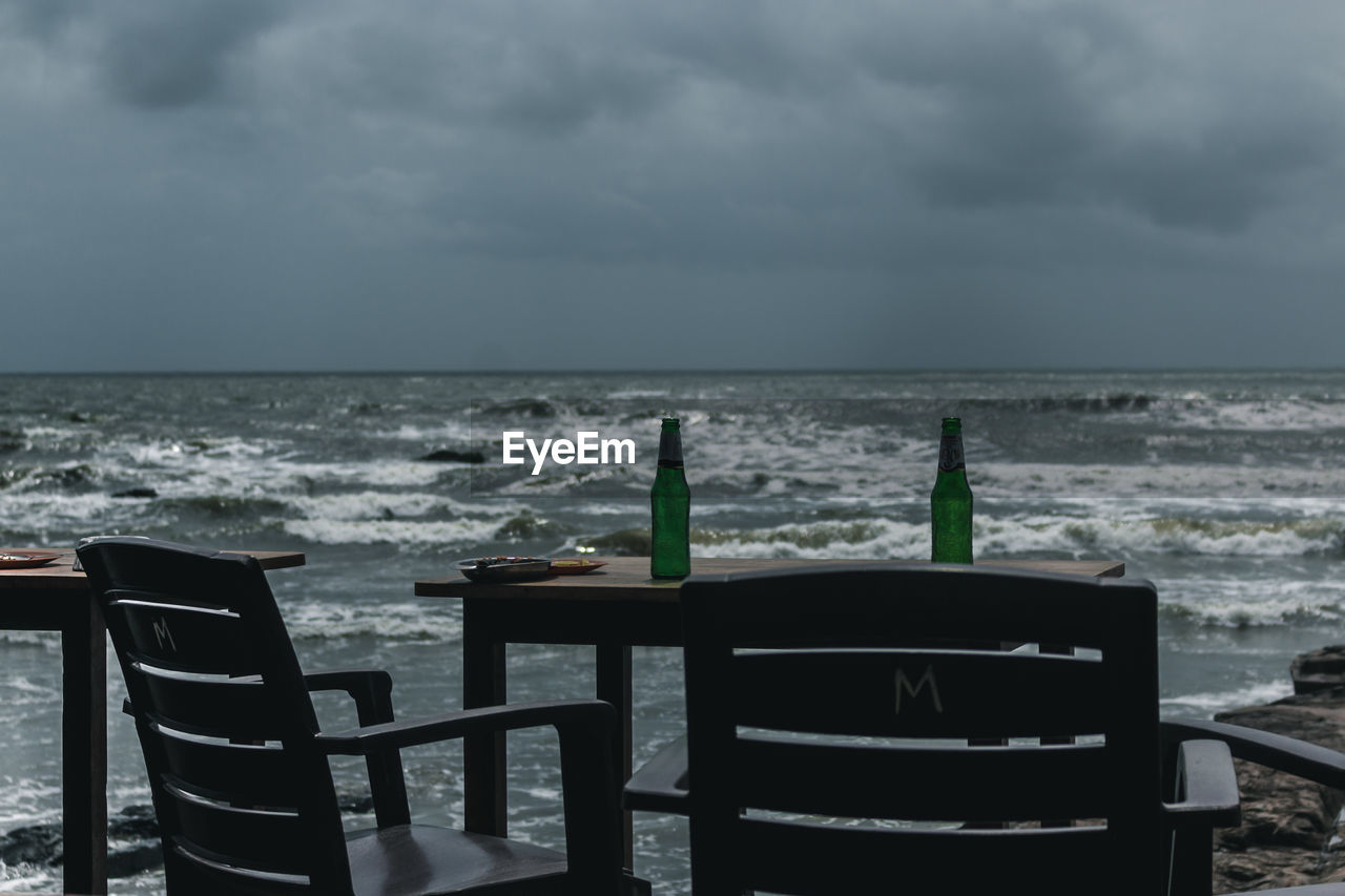 EMPTY CHAIRS AND TABLES ON BEACH AGAINST SKY