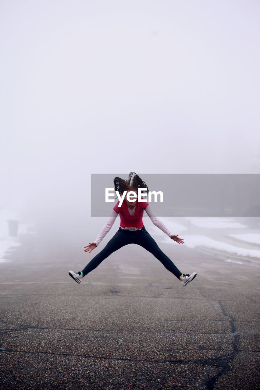 Portrait of young woman jumping on road during foggy weather