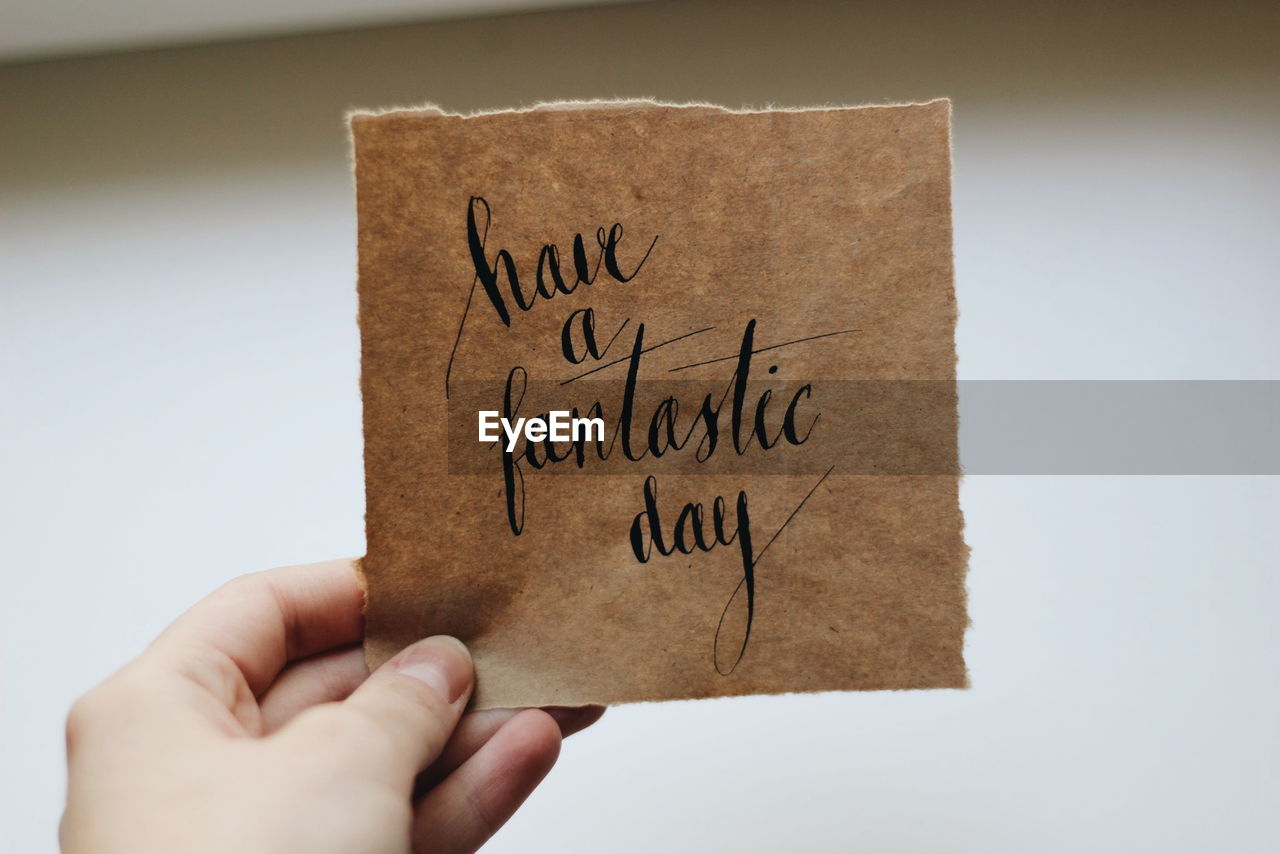 Cropped image of person holding message against white wall