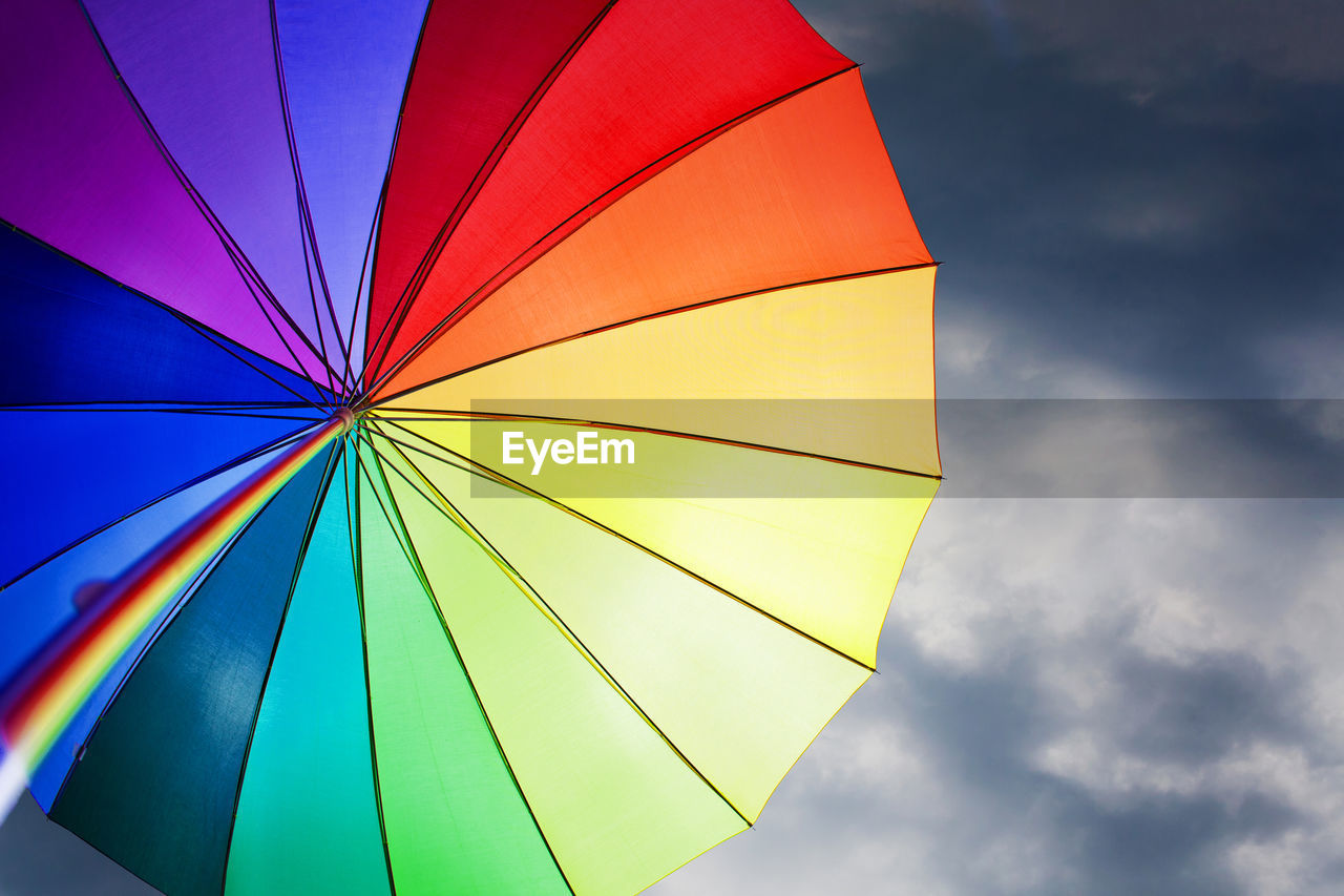 Low angle view of rainbow colored umbrella against blue sky