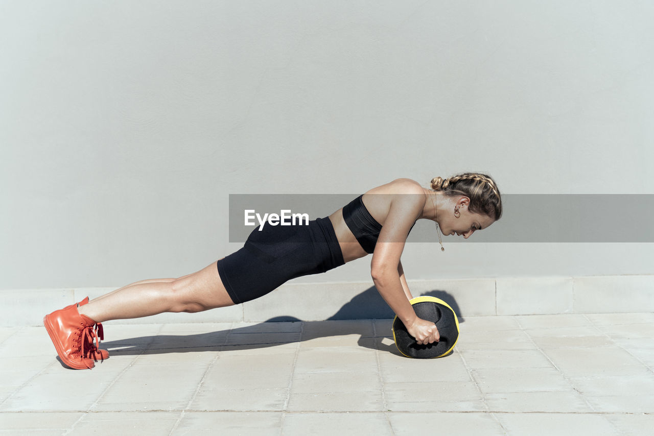 Young woman with medicine ball doing push-ups on footpath