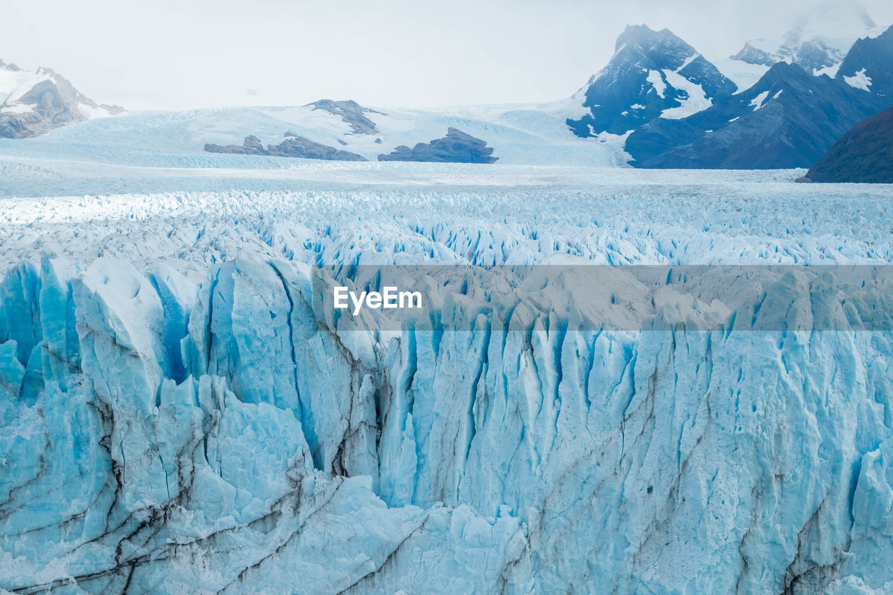 Glacier against snowcapped mountains and cloudy sky