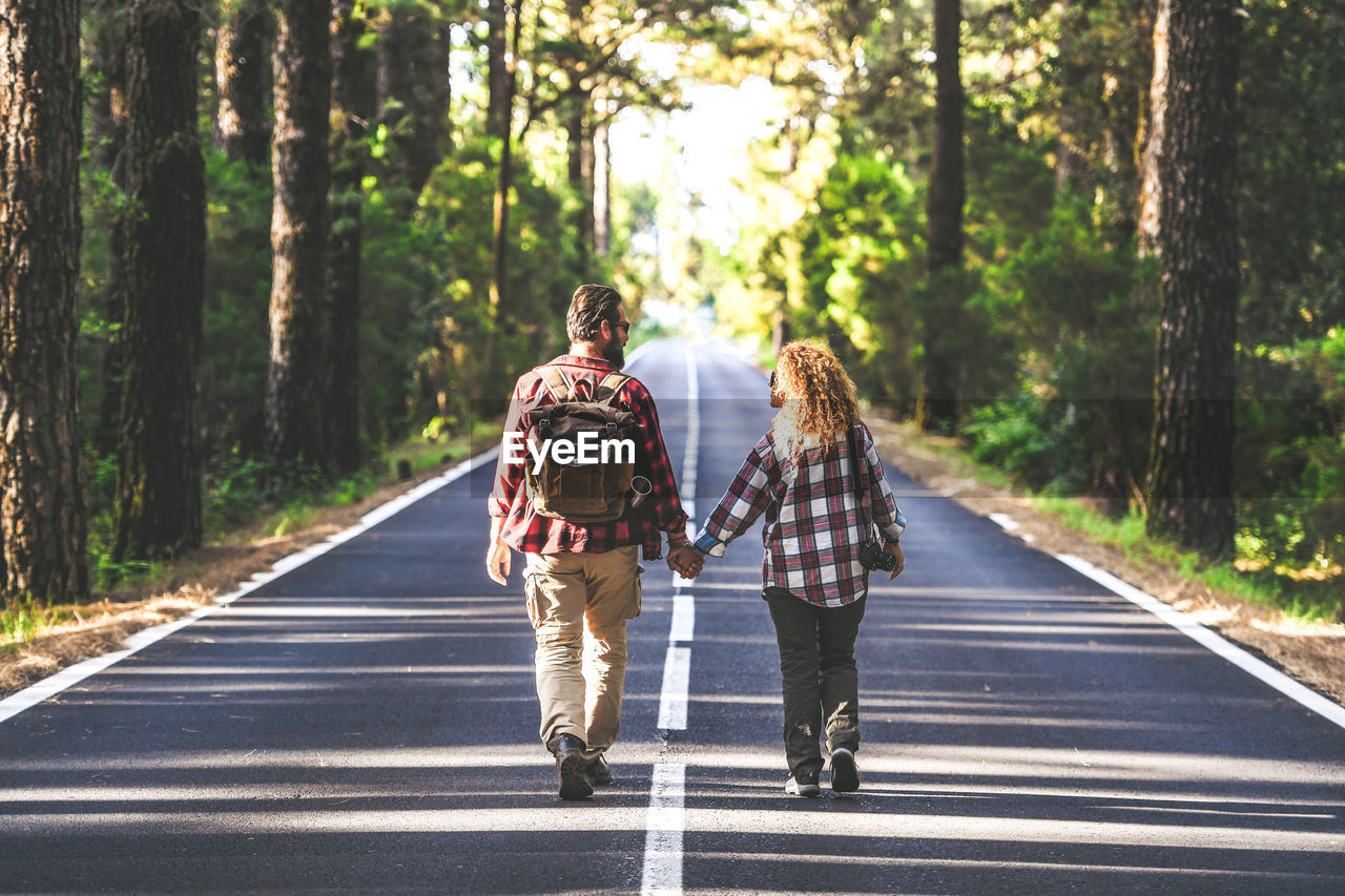 Rear view of couple holding hands while walking on road in forest