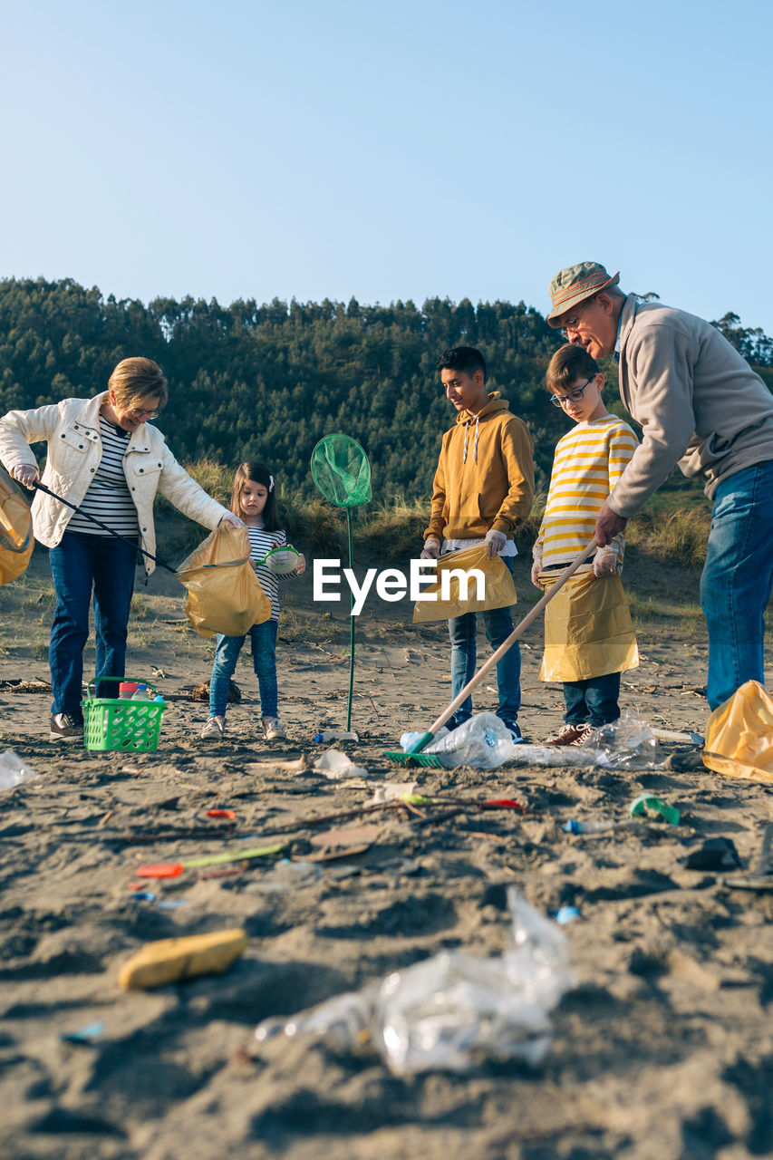 Grandparents and grandchildren cleaning while standing at beach