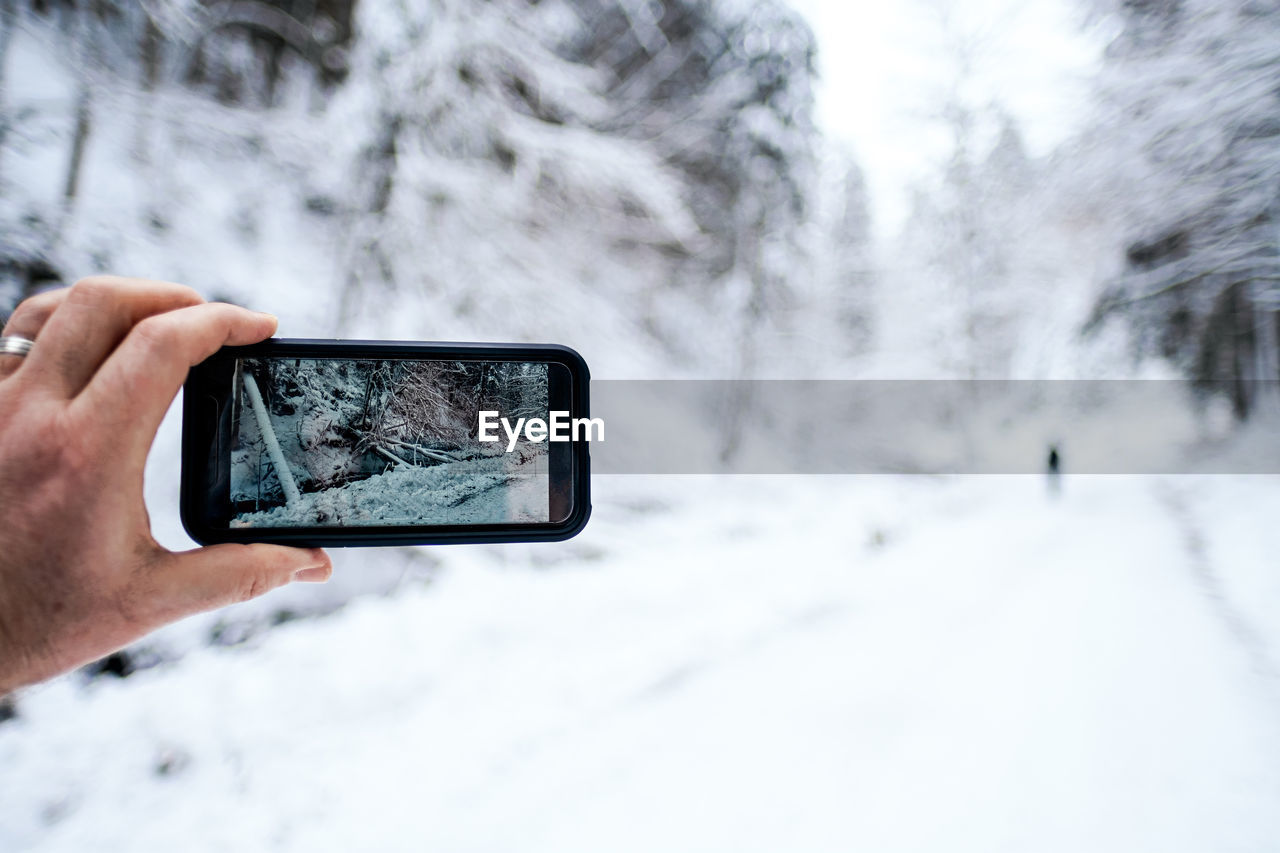 Midsection of person photographing with smartphone in snow covered landscape