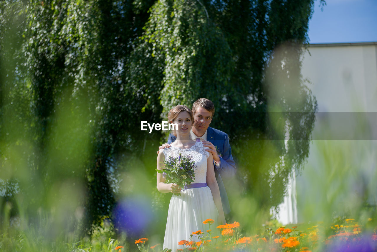 Bride and groom seen through plants at park