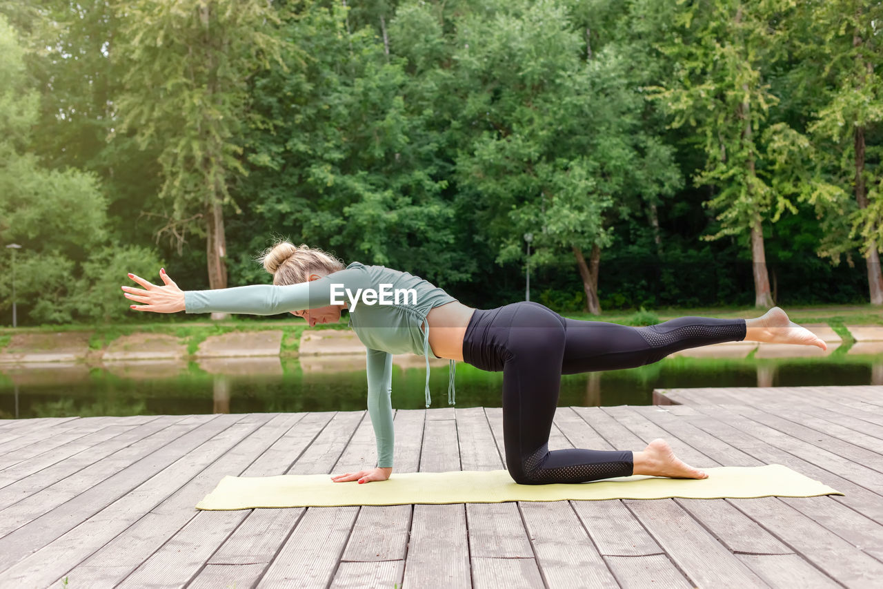 A slender woman on a wooden platform in summer, does yoga