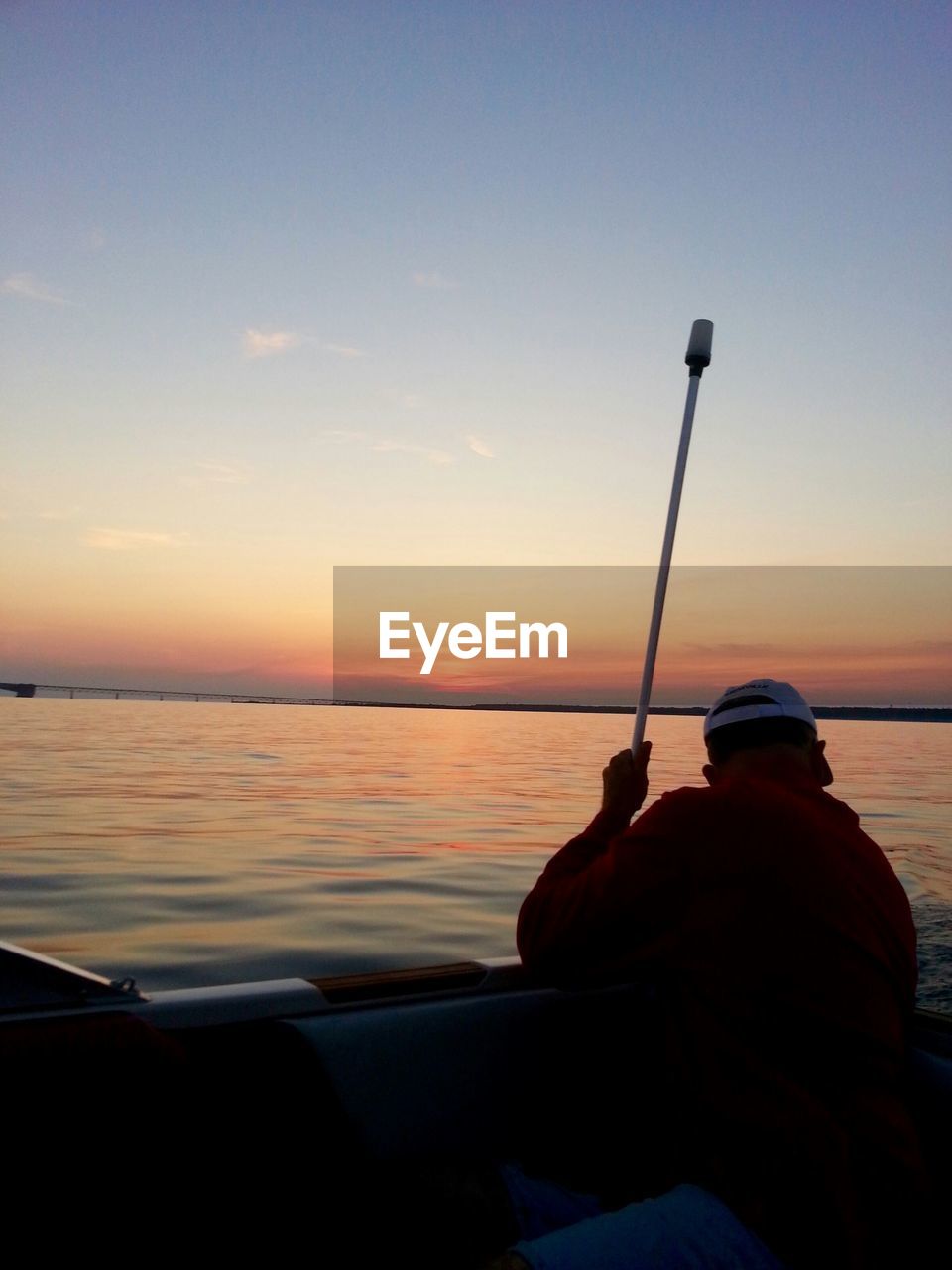 Rear view of man boating in river against clear sky at sunset