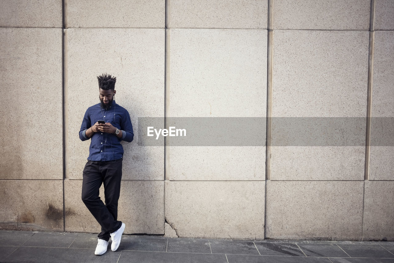 Man listening to music from mobile phone against wall