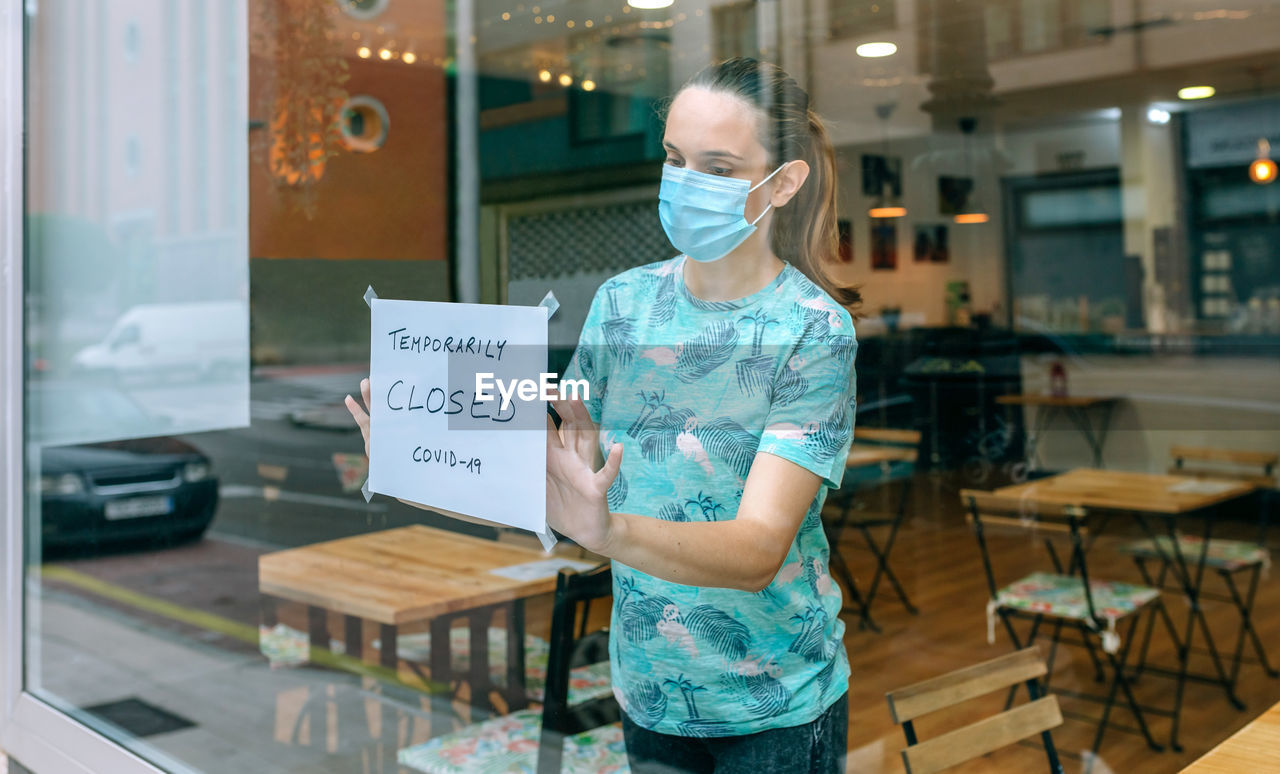 Woman wearing mask placing sign on glass