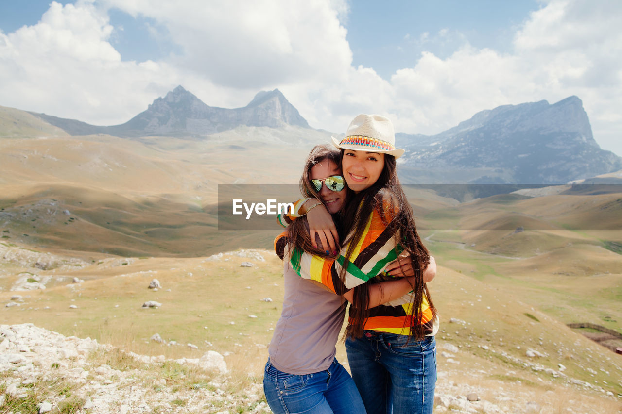 Portrait of friends embracing on landscape against sky