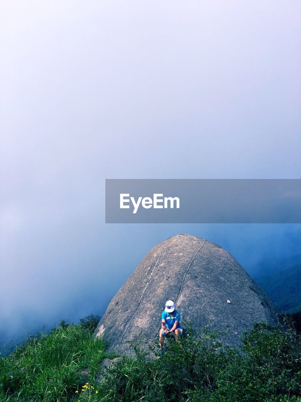 High angle view of hiker sitting on rock while using phone in foggy weather