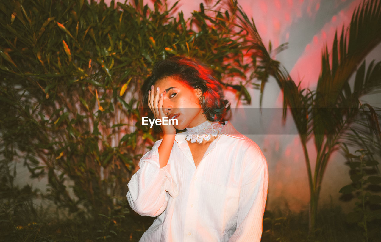 Portrait of beautiful young woman sitting against plants