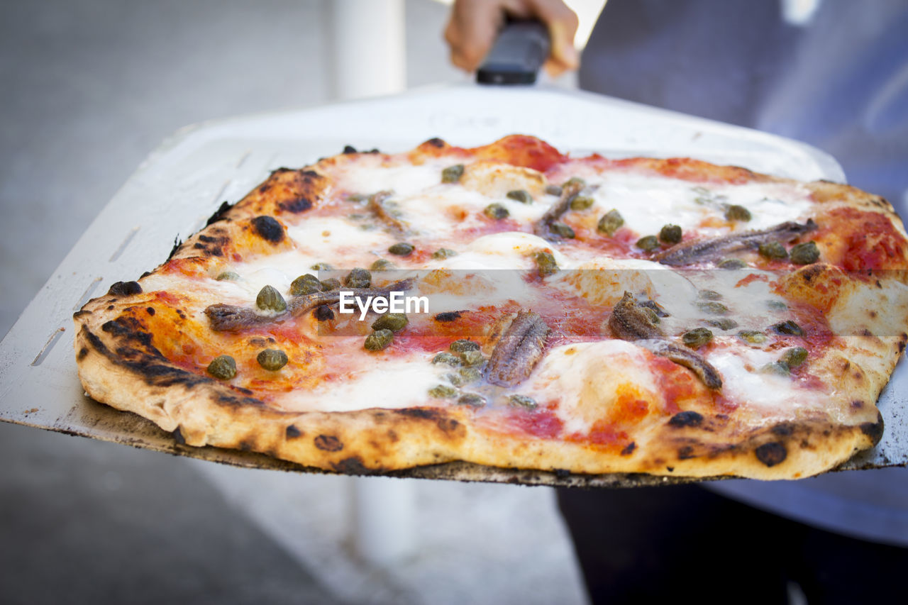 pizza, food, food and drink, italian food, fast food, dish, cuisine, cheese, freshness, dairy, unhealthy eating, vegetable, restaurant, close-up, business, indoors, fast food restaurant, take out food, olive, one person, focus on foreground, meal, mozzarella, high angle view, baked, slice, occupation, fruit