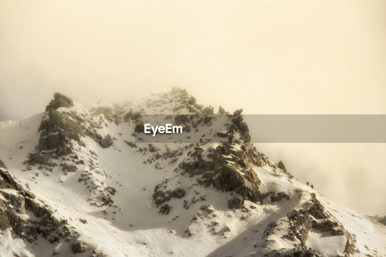 Scenic view of snow covered mountains with climbers against sky 