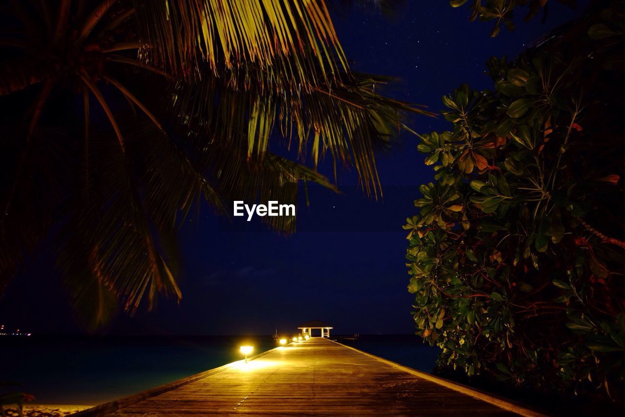 Illuminated pier over sea against sky at night