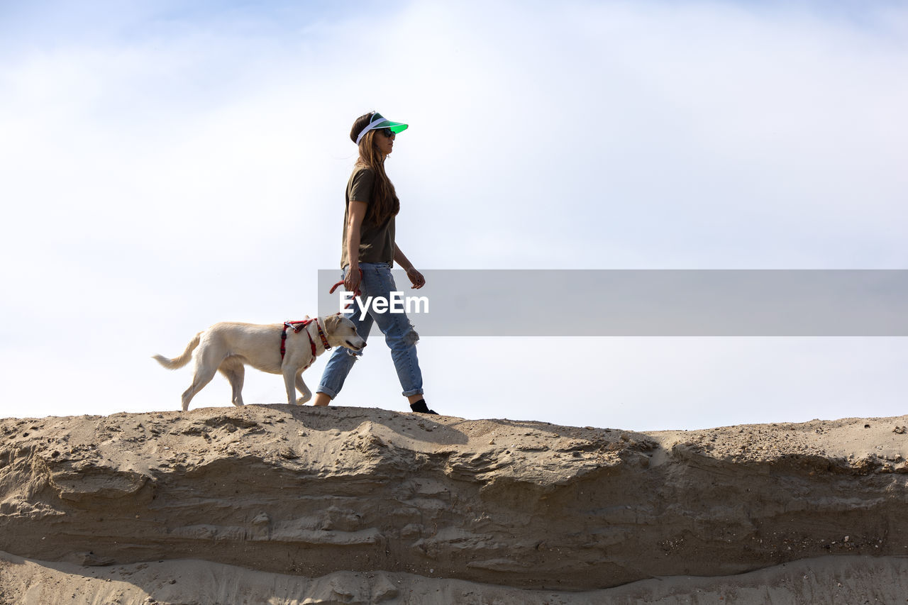 Young woman walking with her dog on the sand in desert