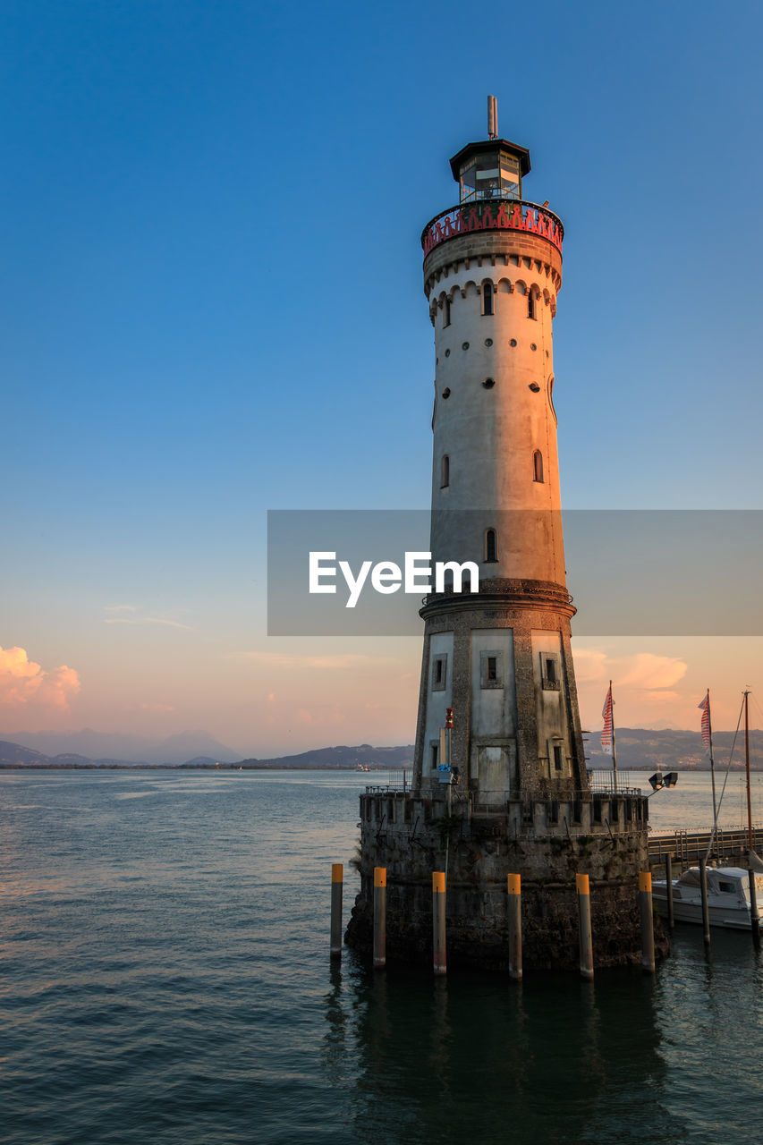 Lighthouse by sea against sky during sunset